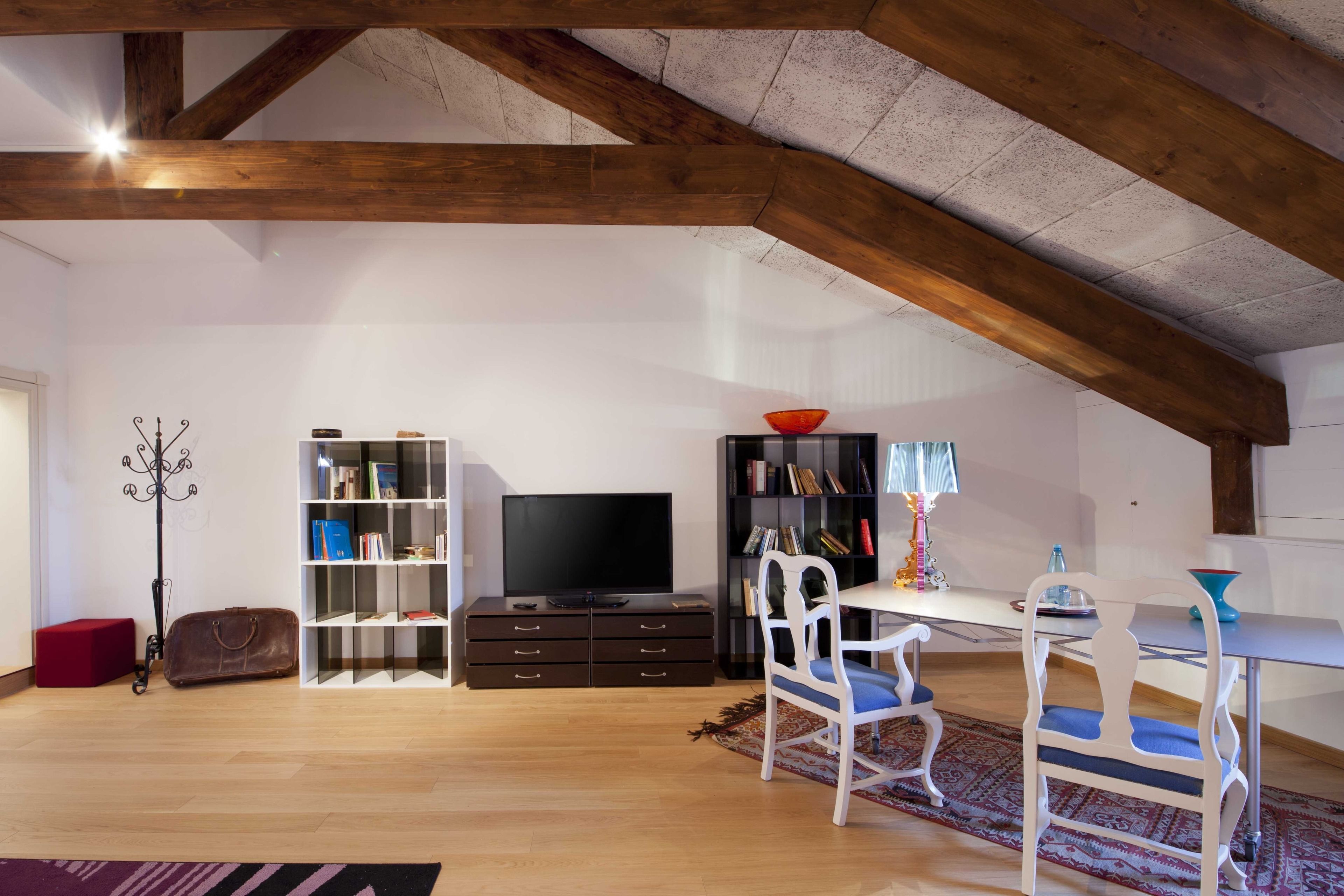 A modern living room with a wooden ceiling, a bookshelf, a TV, and a dining area with chairs and a table.