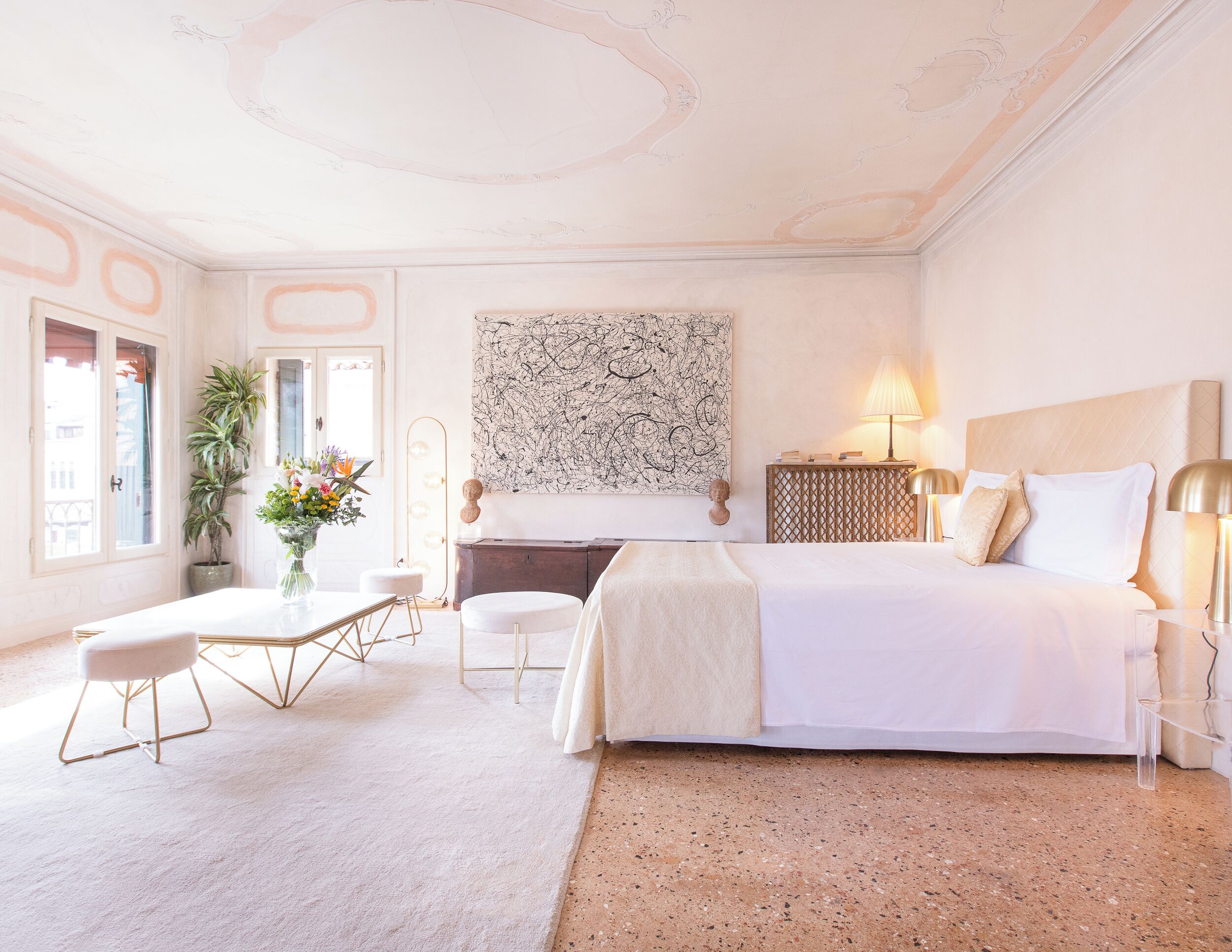 A hotel room with a bed, bedside table, lamp, and a large abstract painting on the wall.