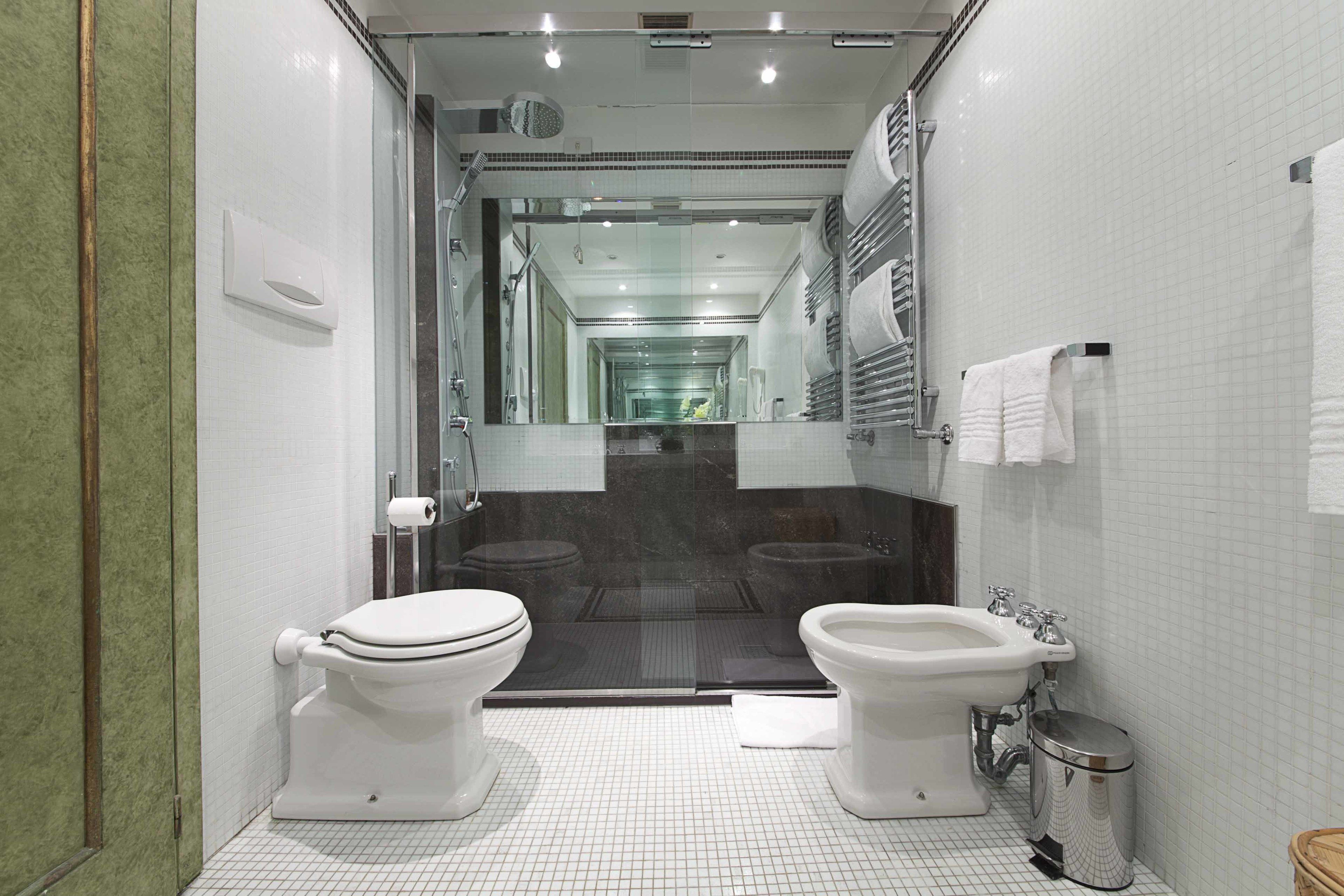 Un baño moderno con dos inodoros, un bidé, un cubo de basura y una ducha con mampara de cristal.