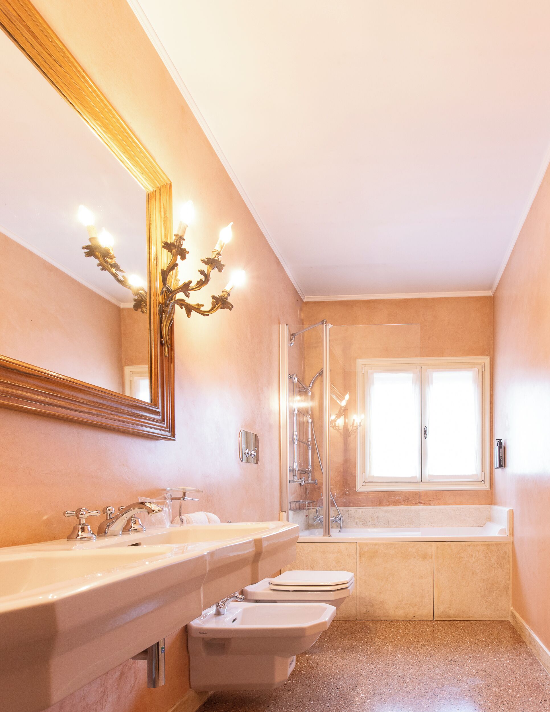 A bathroom with a large mirror, two sinks, a shower, and a toilet.