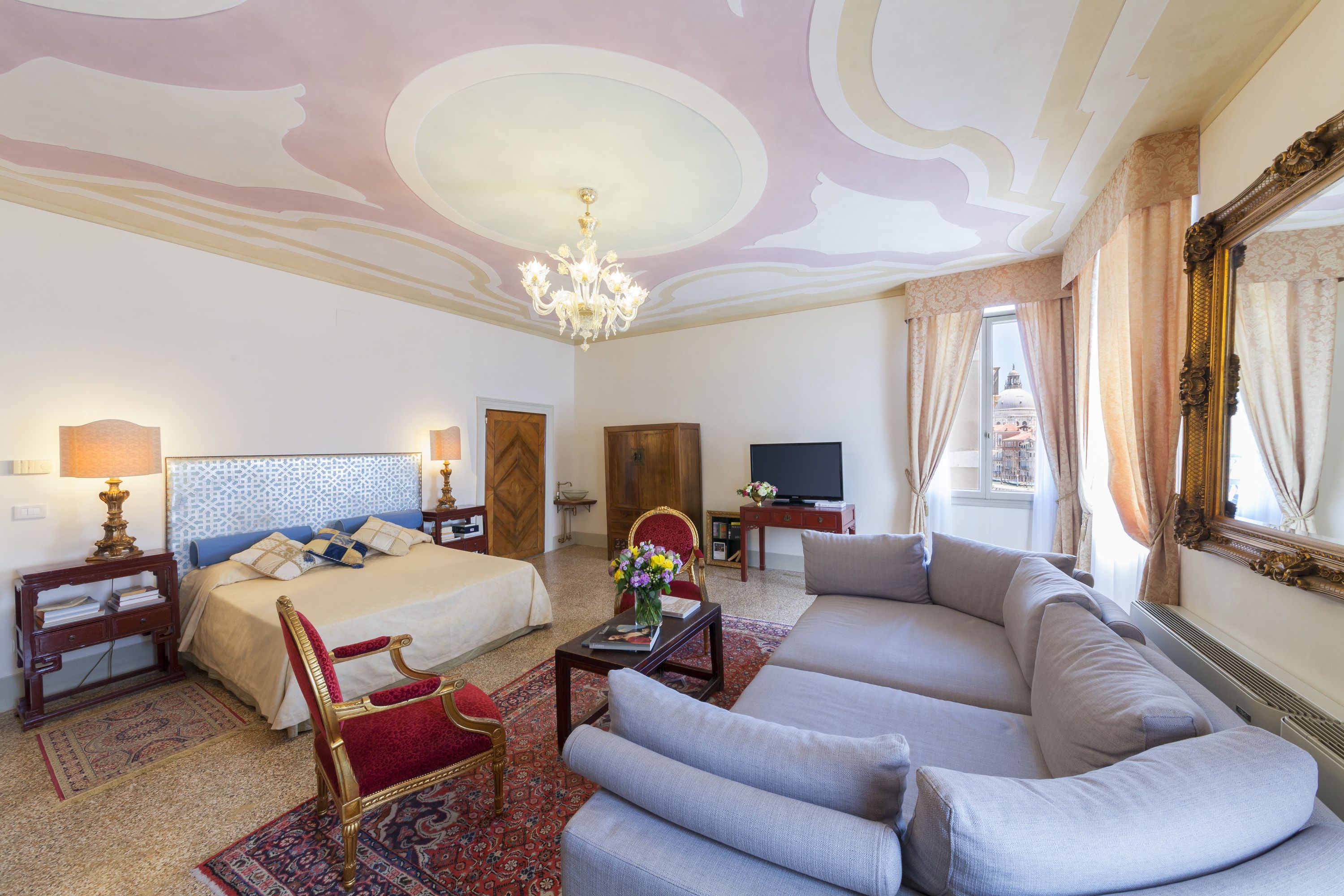 A hotel room with a bed, a sofa, a TV, and a chandelier.