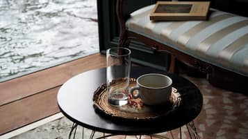Une table avec un verre et une tasse, un livre posé sur un banc rembourré, et une vue sur l’eau à l’extérieur.