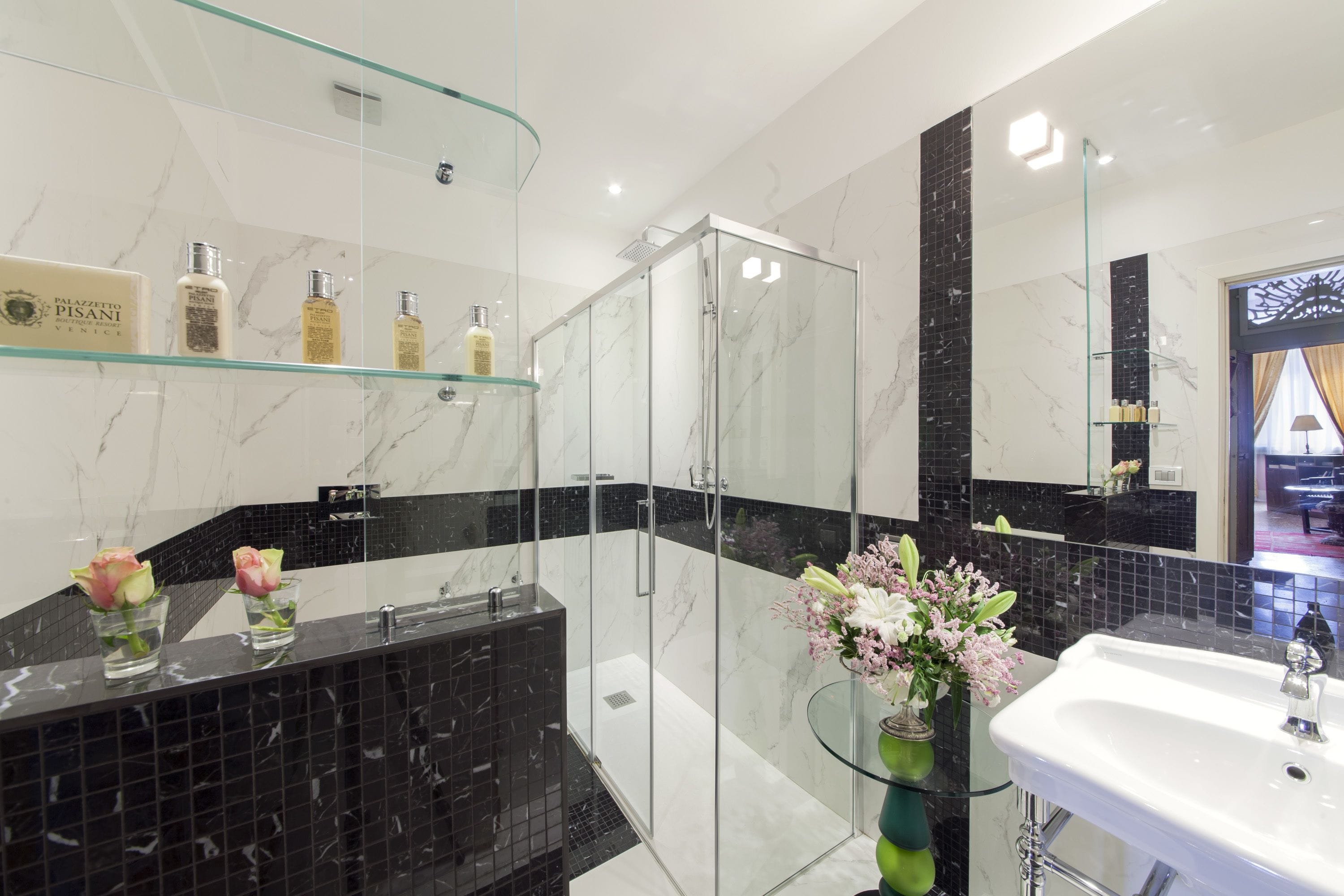 Um banheiro moderno com box de vidro, azulejos de mármore e prateleira de vidro com artigos de higiene pessoal.