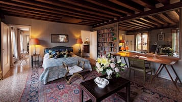 A cozy bedroom with a large bed, a wooden desk, a bookshelf, and a patterned rug.