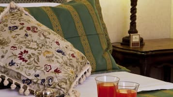 A neatly arranged breakfast tray with a silver pitcher, cups, and glasses of tea on a bed with green and floral pillows.