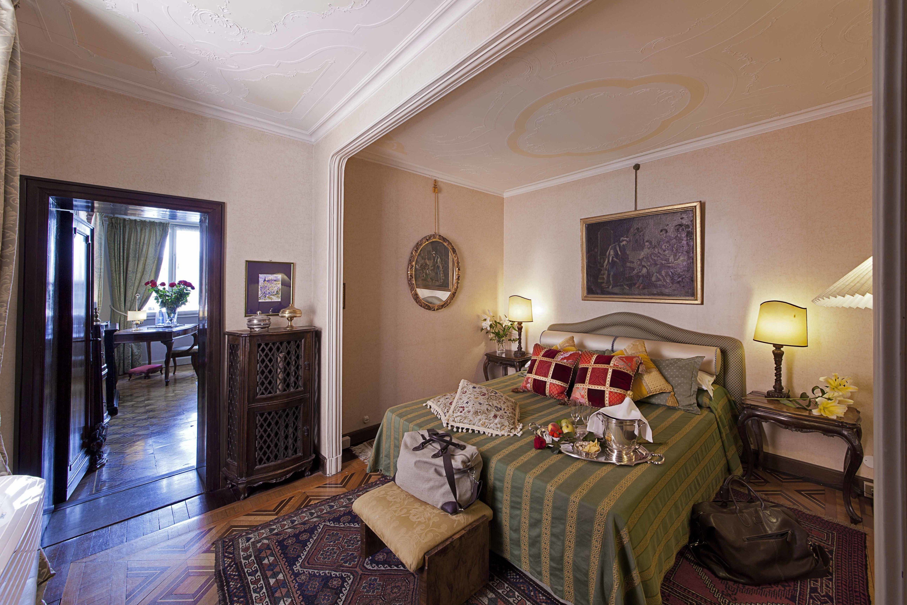 A hotel room with a bed, bedside tables, a mirror, a painting, and a view of the hallway.