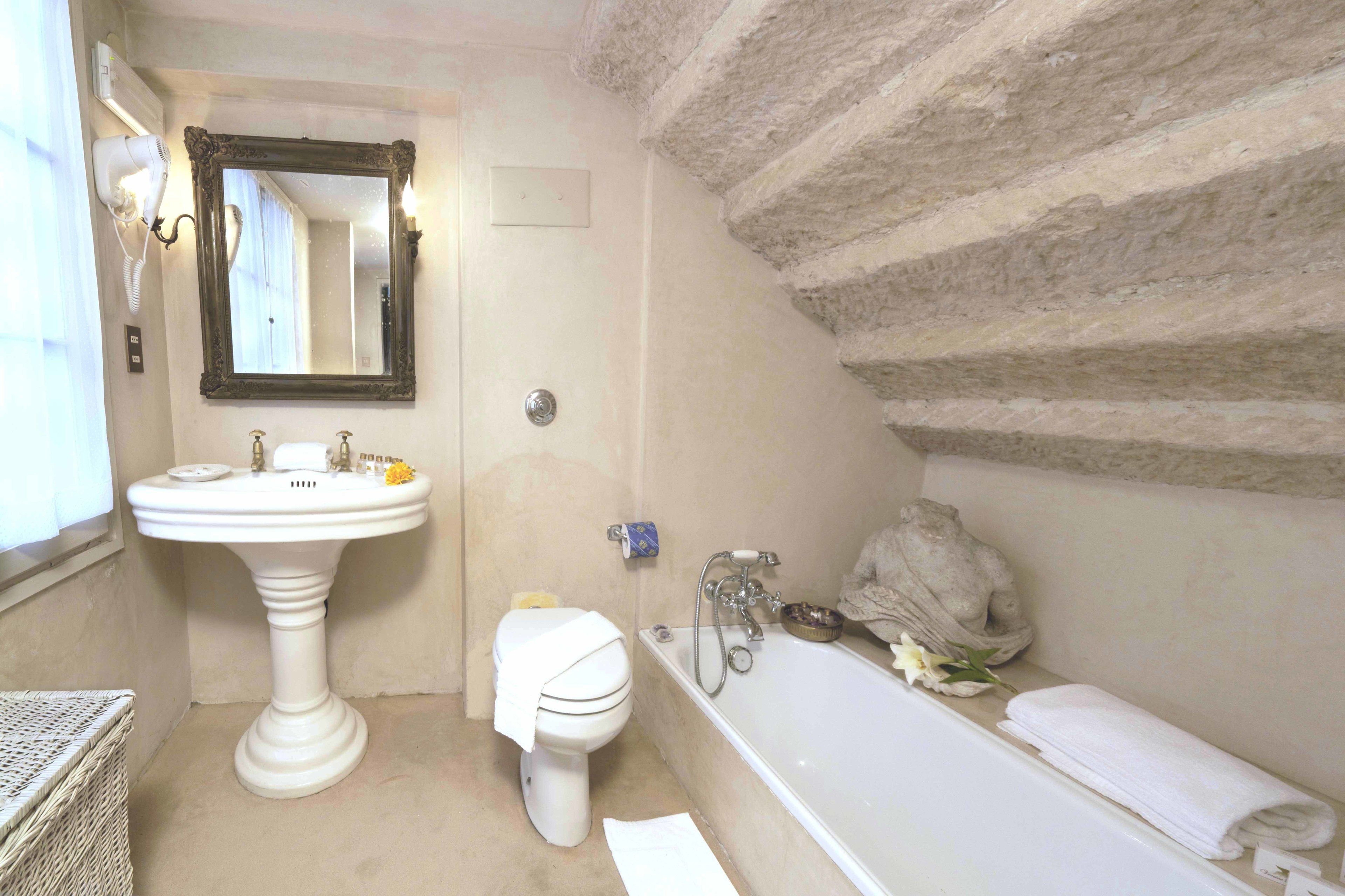 Une salle de bain avec un lavabo sur colonne, des toilettes, une baignoire et un mur en pierre.