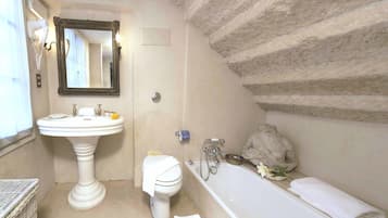 A bathroom with a pedestal sink, a toilet, a bathtub, and a stone wall.