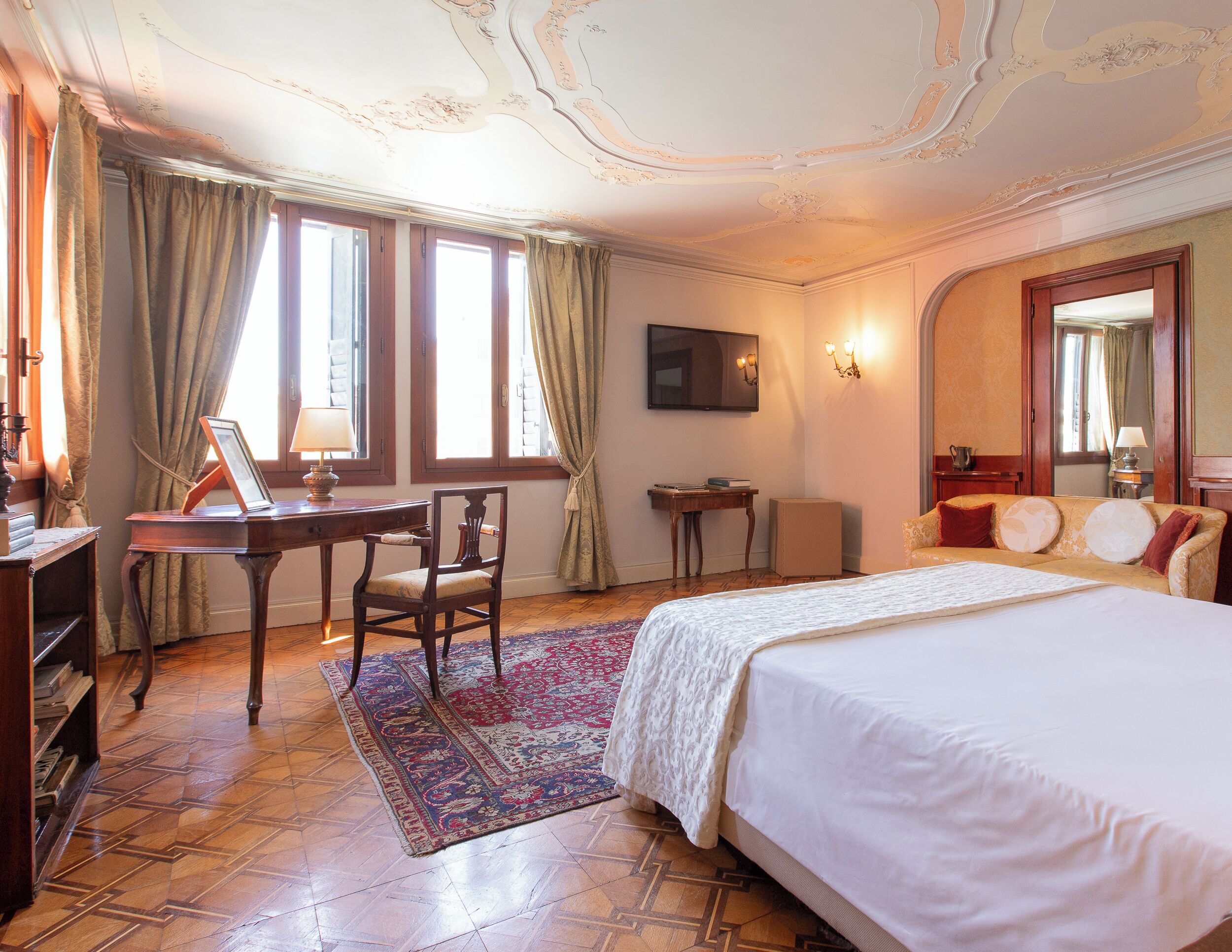 A hotel room with a large bed, a desk, a chair, a small table, and a television.