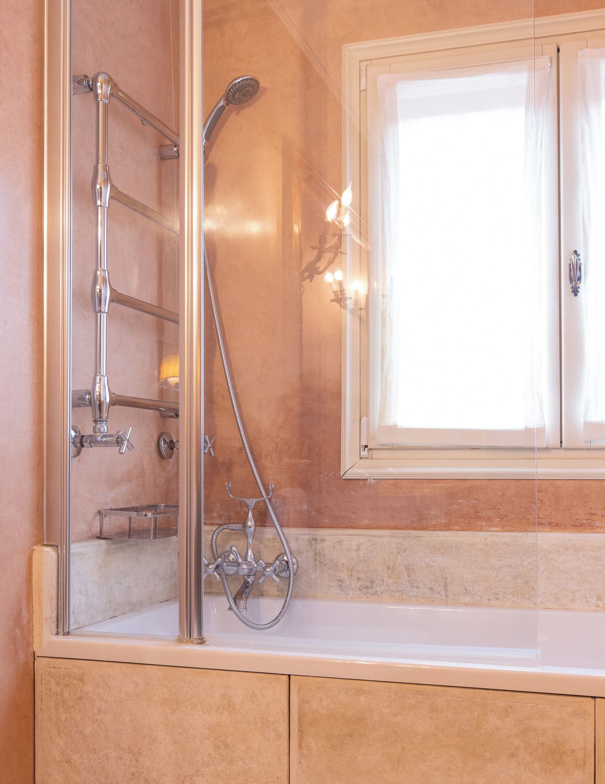Un baño con ducha de vidrio, bañera y ventana con cortinas.