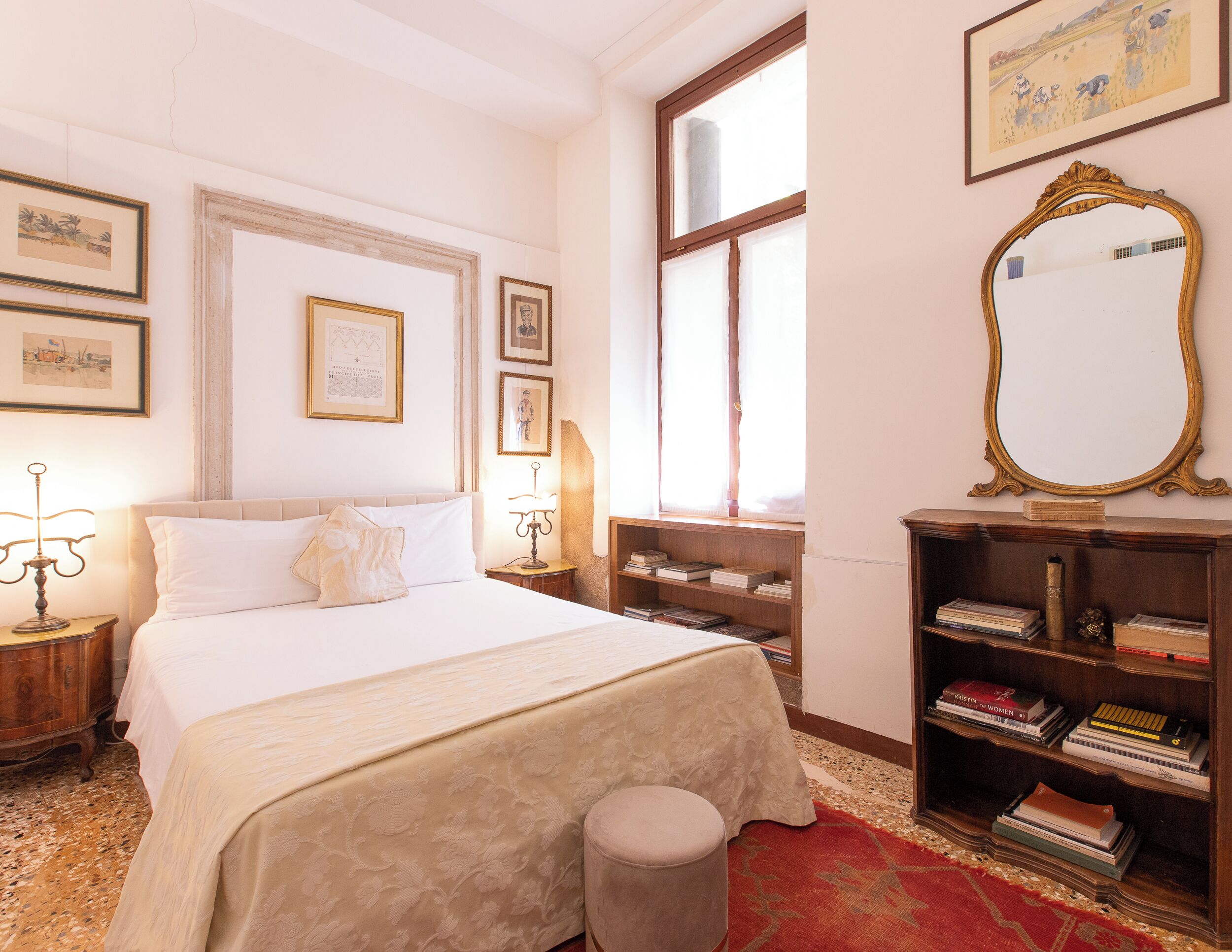 A neatly arranged bedroom with a large bed, bedside tables, a bookshelf, and a mirror.