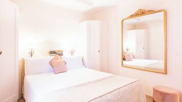 Una habitación de hotel con una cama grande, una mesita de noche con libros, un espejo y un taburete pequeño.