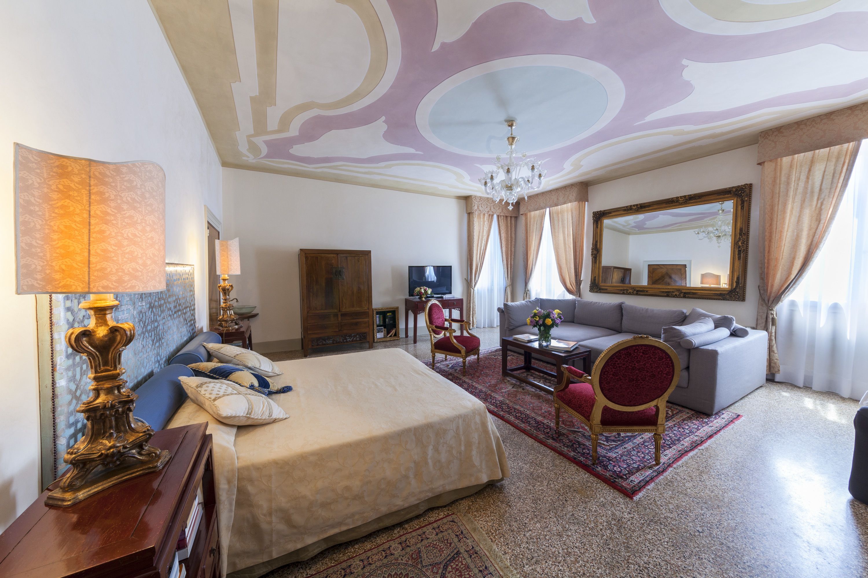 Una habitación de hotel con una cama grande, un sofá, un televisor y una araña.