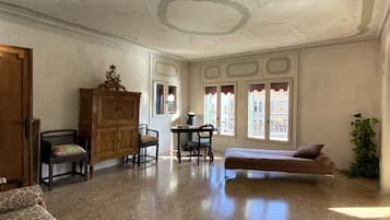A spacious room with a polished floor, a wooden cabinet, a sofa, a dining table with chairs, and a bed.
