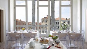 A dining area with clear chairs and a table set for breakfast, overlooking a cityscape with historic buildings. - Palazzetto Pisani (Venice)
