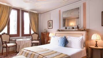 A hotel room with a large bed, two bedside tables, a small round table, a chair, and a large mirror above the bed.