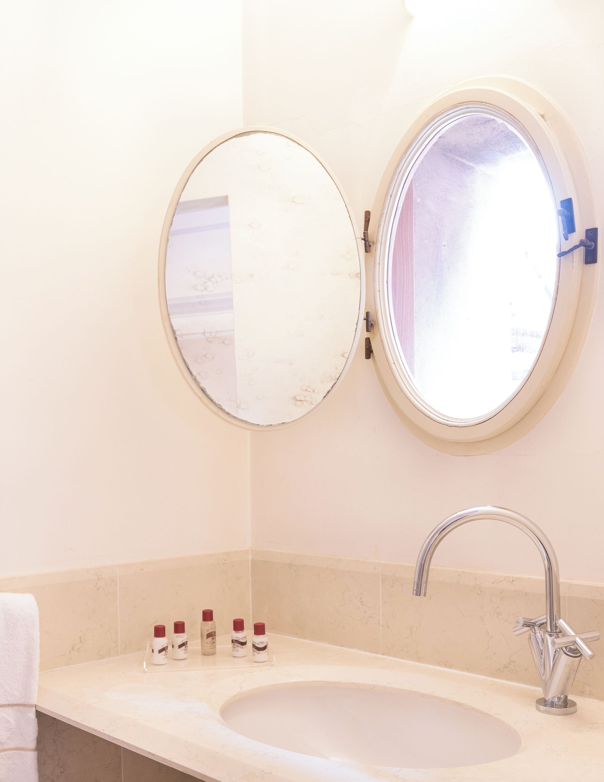 A bathroom with a round mirror, a sink, and three bottles of toiletries on the countertop.