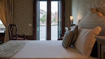 A hotel room with a bed, a chair, a lamp, and a view of a cityscape through an open door.
