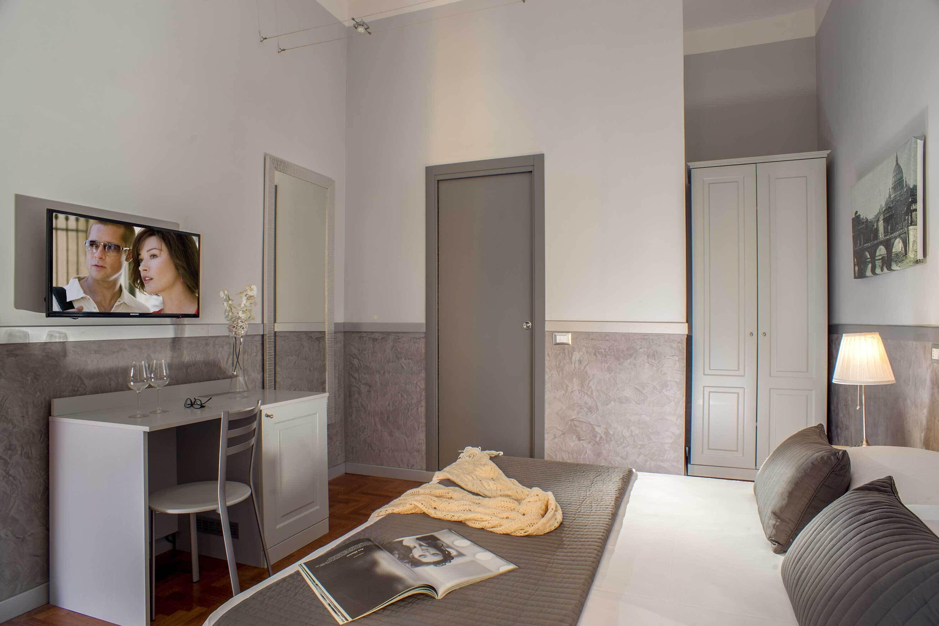 A hotel room with a bed, a desk, a chair, a TV, and a wardrobe.