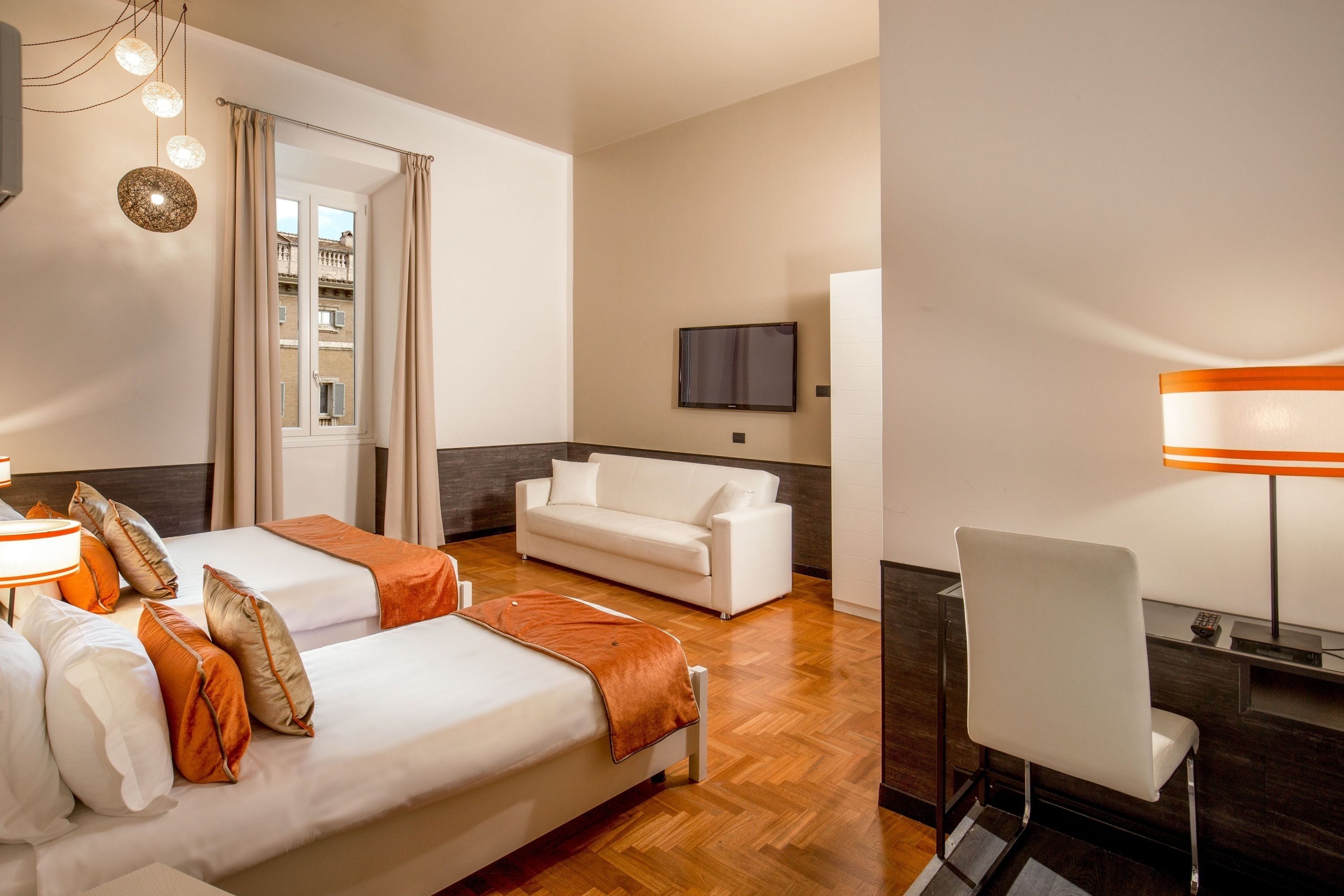 A hotel room with two beds, a sofa, a desk, and a TV.