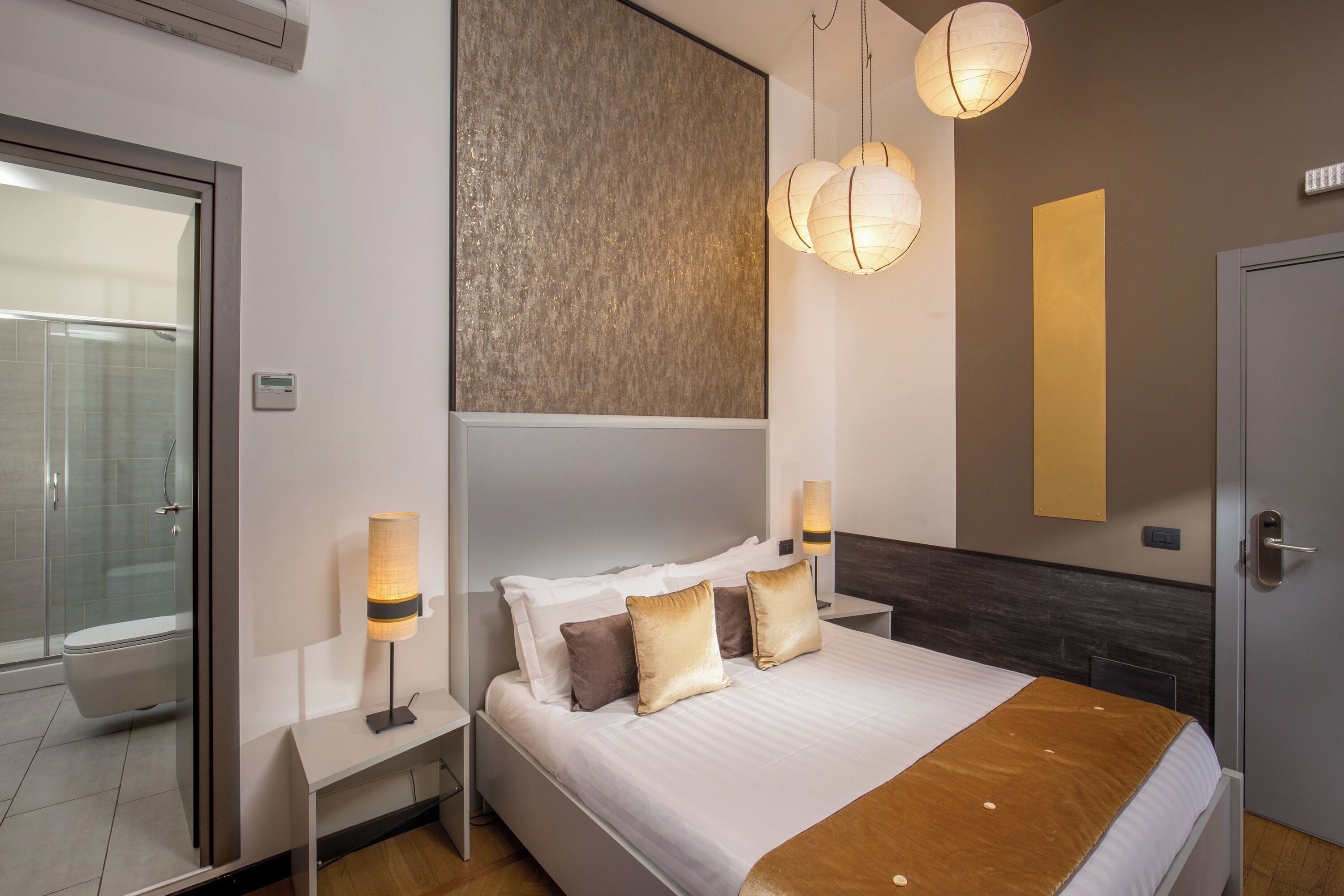 A modern hotel room with a large bed, bedside lamps, a nightstand, a wooden headboard, and a large mirror.