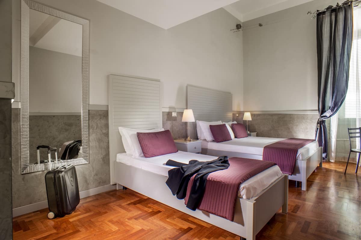 A hotel room with two beds, a large mirror, a suitcase, and a chair.