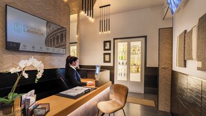 Ein Hotel-Empfangsbereich mit einem digitalen Bildschirm, der den Hotelnamen anzeigt, einer Rezeption, einer Sitzecke und einer Minibar.