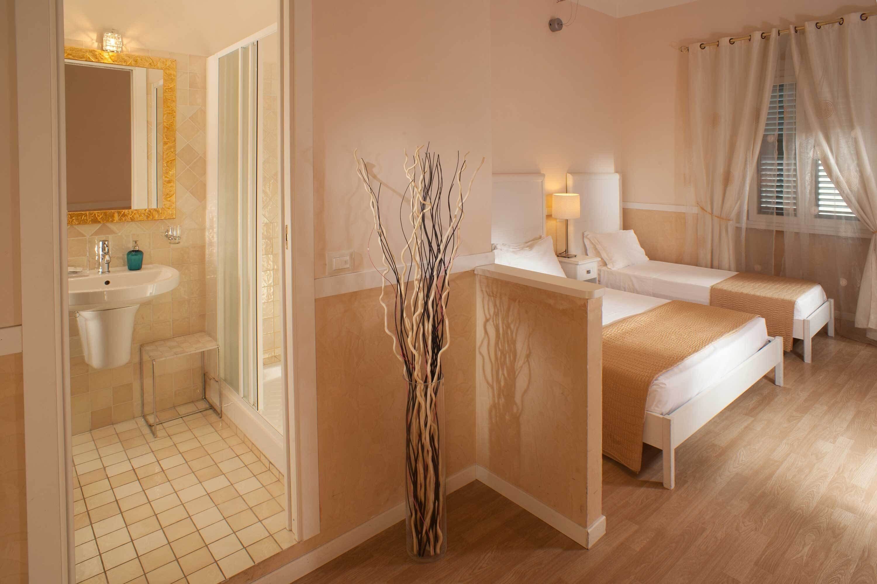 Une chambre d’hôtel avec salle de bain, deux lits, une table de chevet, une lampe et un vase décoratif.