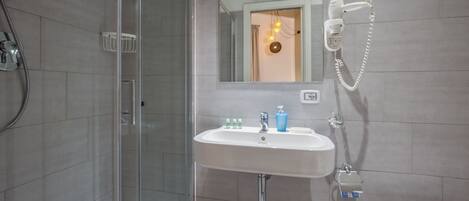 Un baño con ducha acristalada, lavamanos con artículos de aseo y un inodoro.