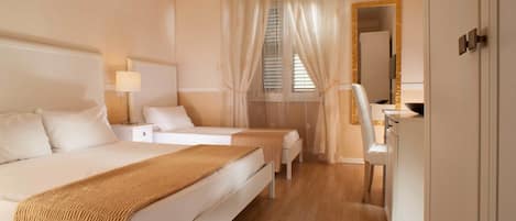 A hotel room with a large bed, two smaller beds, a desk, and a mirror.