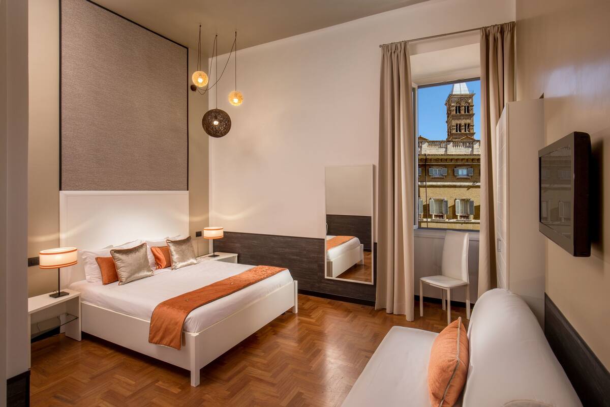 A modern hotel room with a large bed, bedside tables, a desk, a chair, and a large mirror.