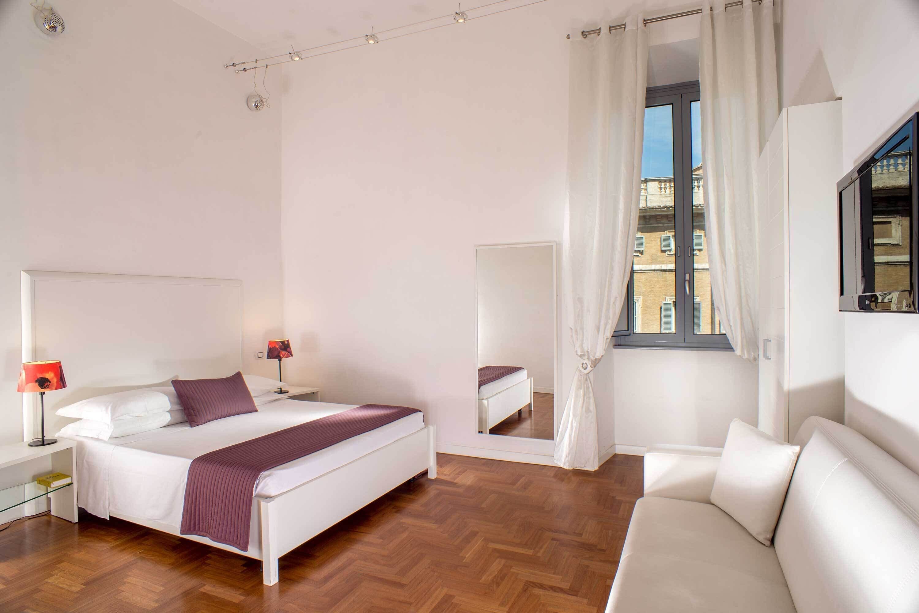 A bedroom with a bed, bedside tables, a mirror, a window with curtains, and a sofa.