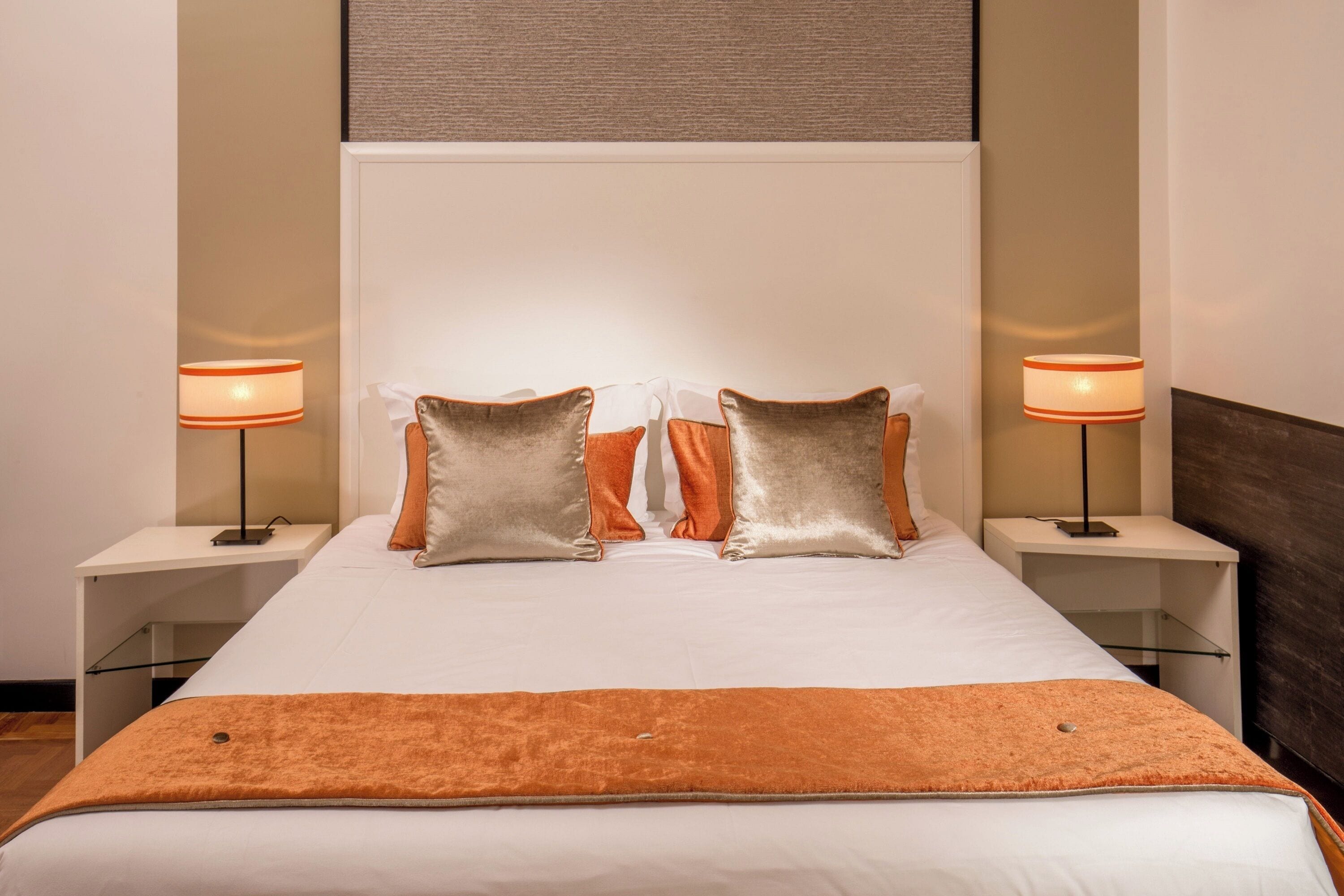 A neatly made bed with two pillows, a bedside table with a lamp, and a wall-mounted shelf.