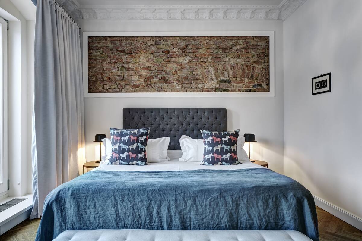 A bedroom with a brick-patterned wall, a tufted headboard, and a blue bedspread.