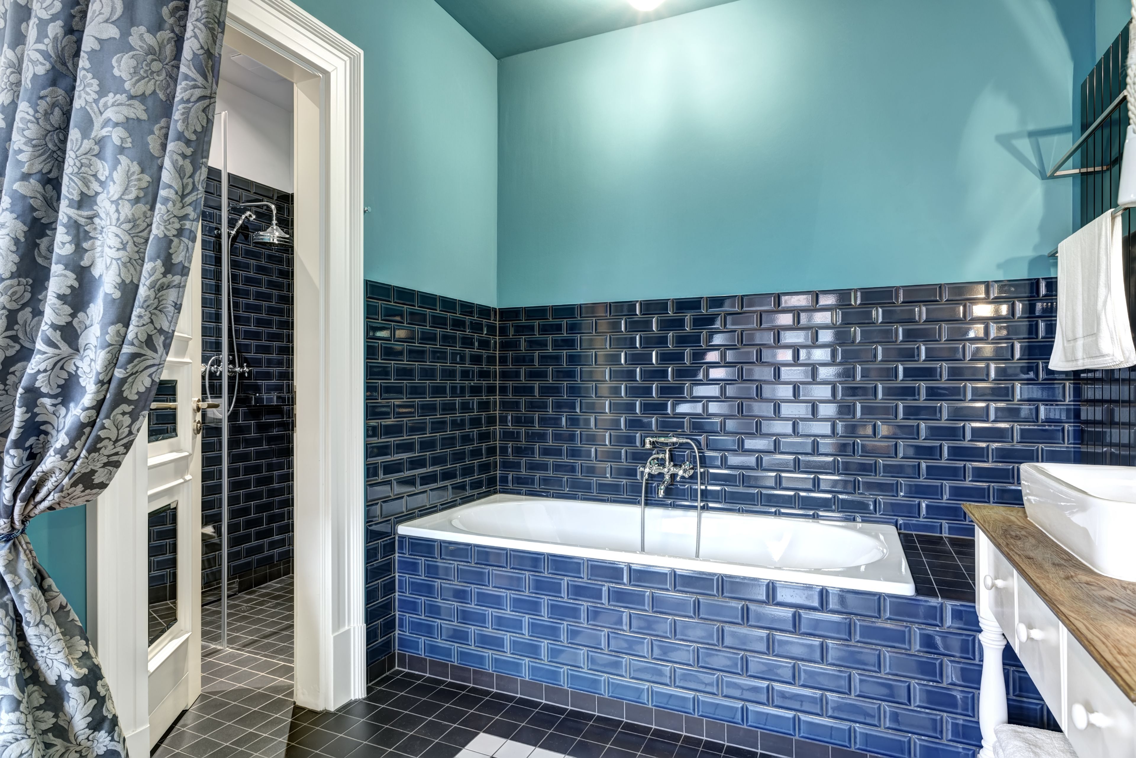 A bathroom with a blue-tiled shower, a white bathtub, and a wooden vanity.