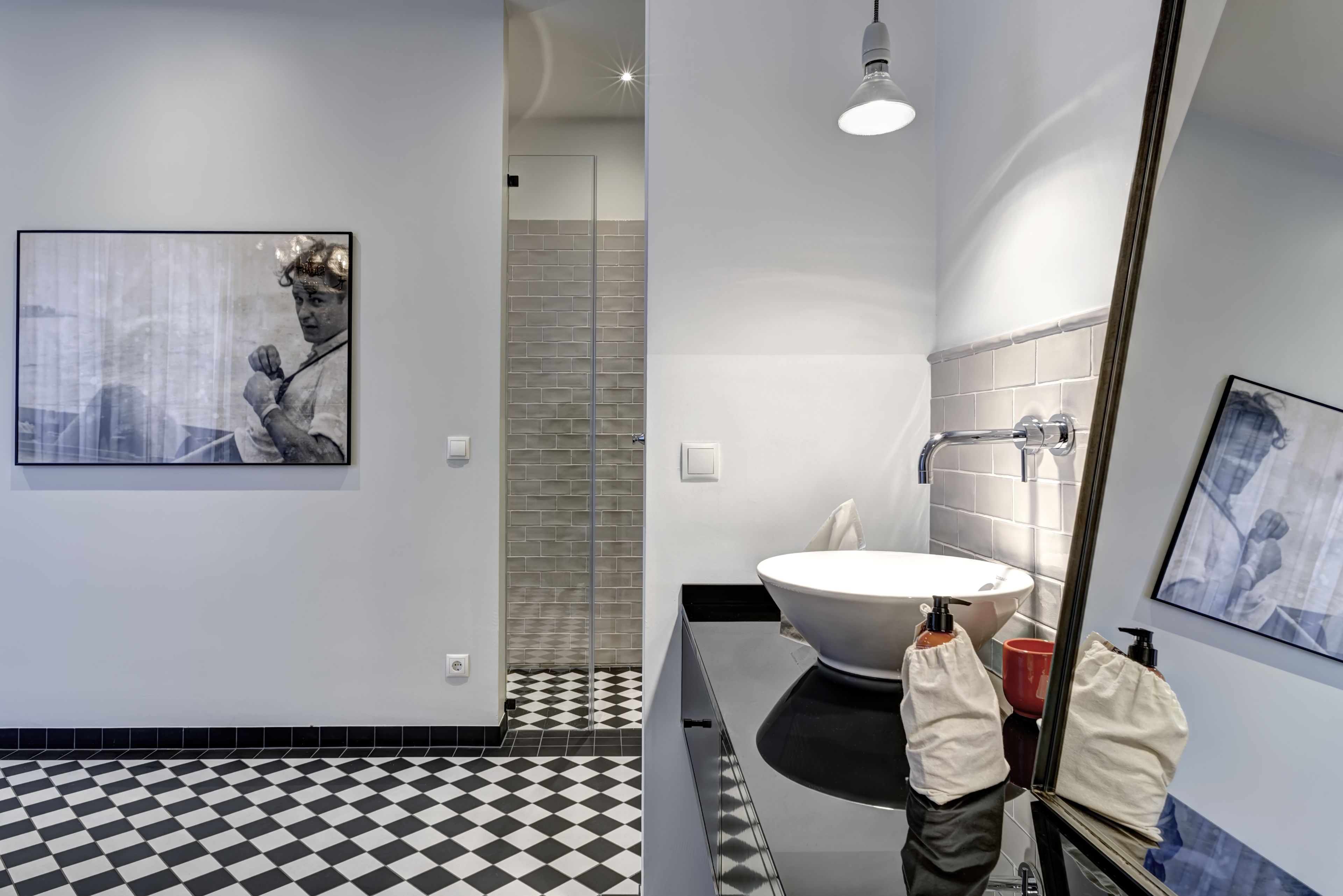 A modern bathroom with a black and white checkered floor, a large mirror, a white sink, and a shower area.