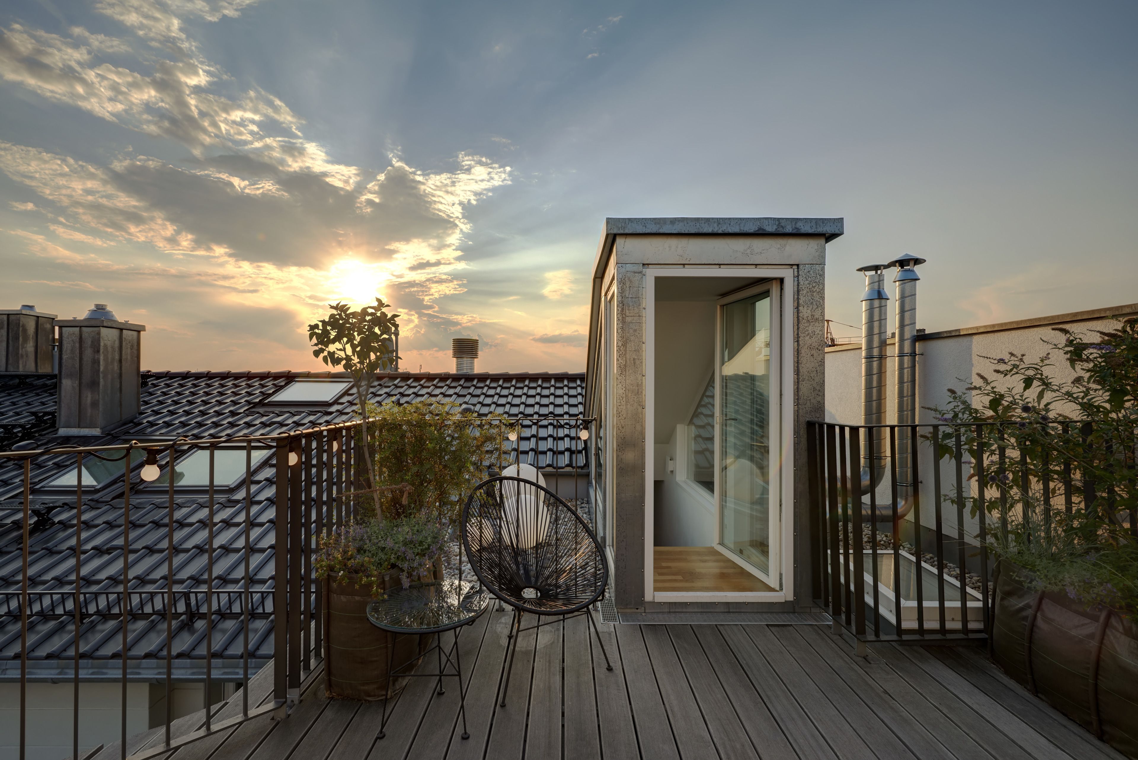 Une terrasse sur le toit au design moderne, dotée d’une porte vitrée donnant sur un espace intérieur, d’une chaise en métal et de plantes en pot.