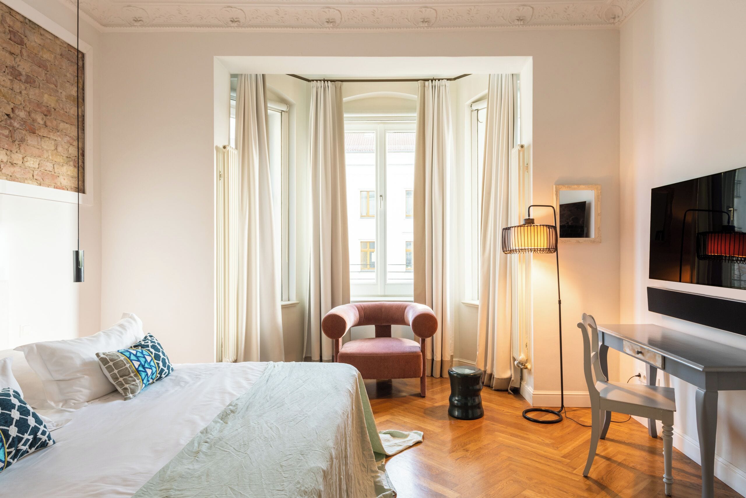 Quarto de hotel com cama, escrivaninha, cadeira e televisão.