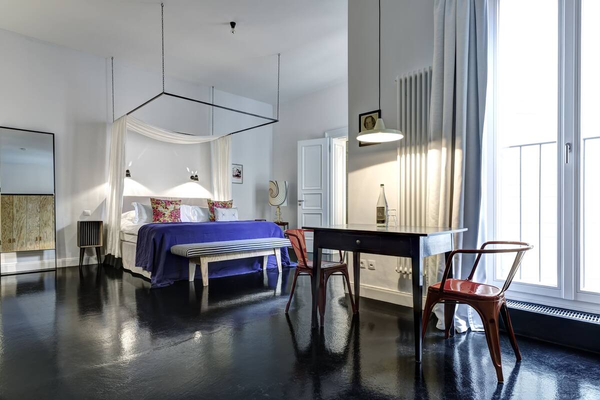 A modern bedroom with a bed, bedside table, chair, and a large window.