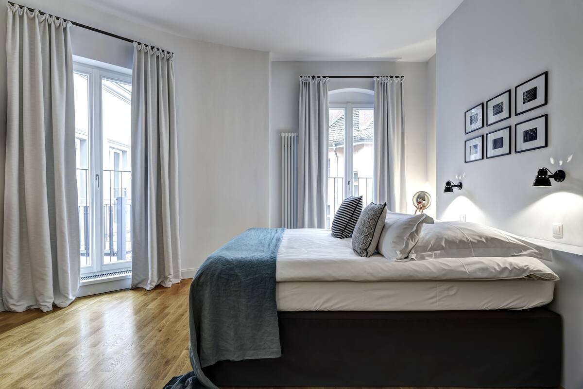 A bedroom with a bed, curtains, a window, and wall-mounted lights.
