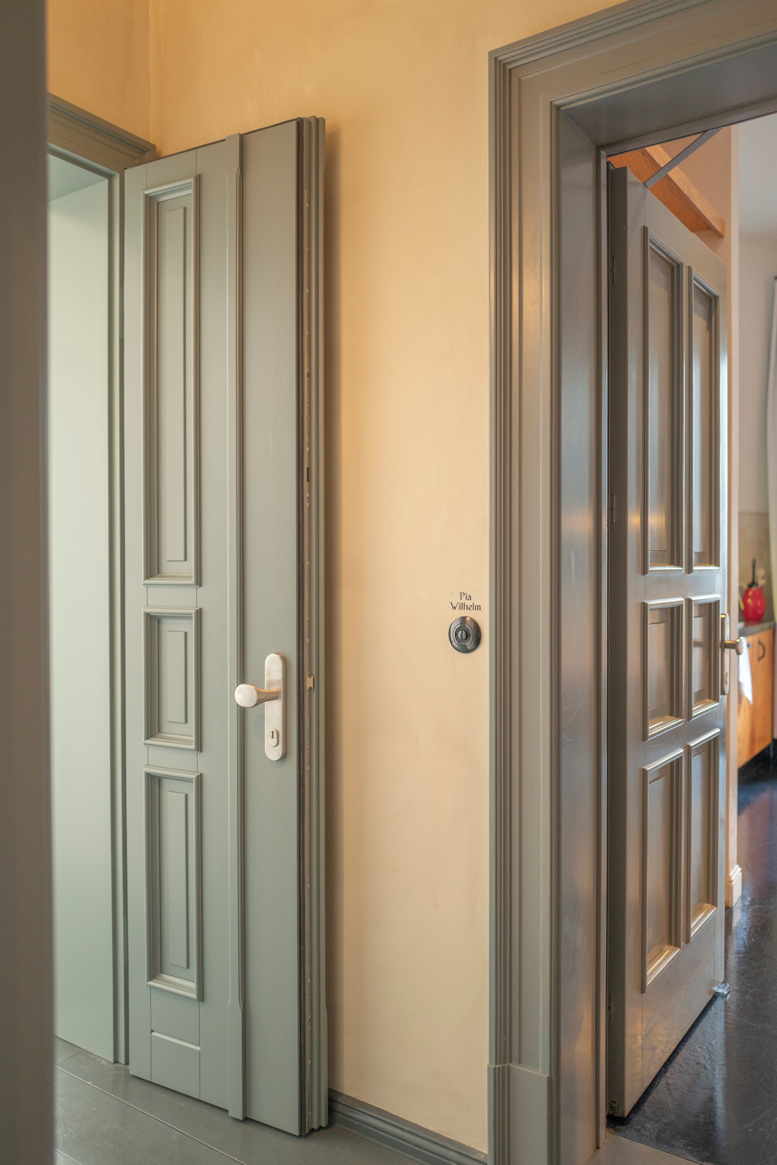 A hallway with double doors, one of which has a lock and a nameplate reading "Pia Wilhelm".