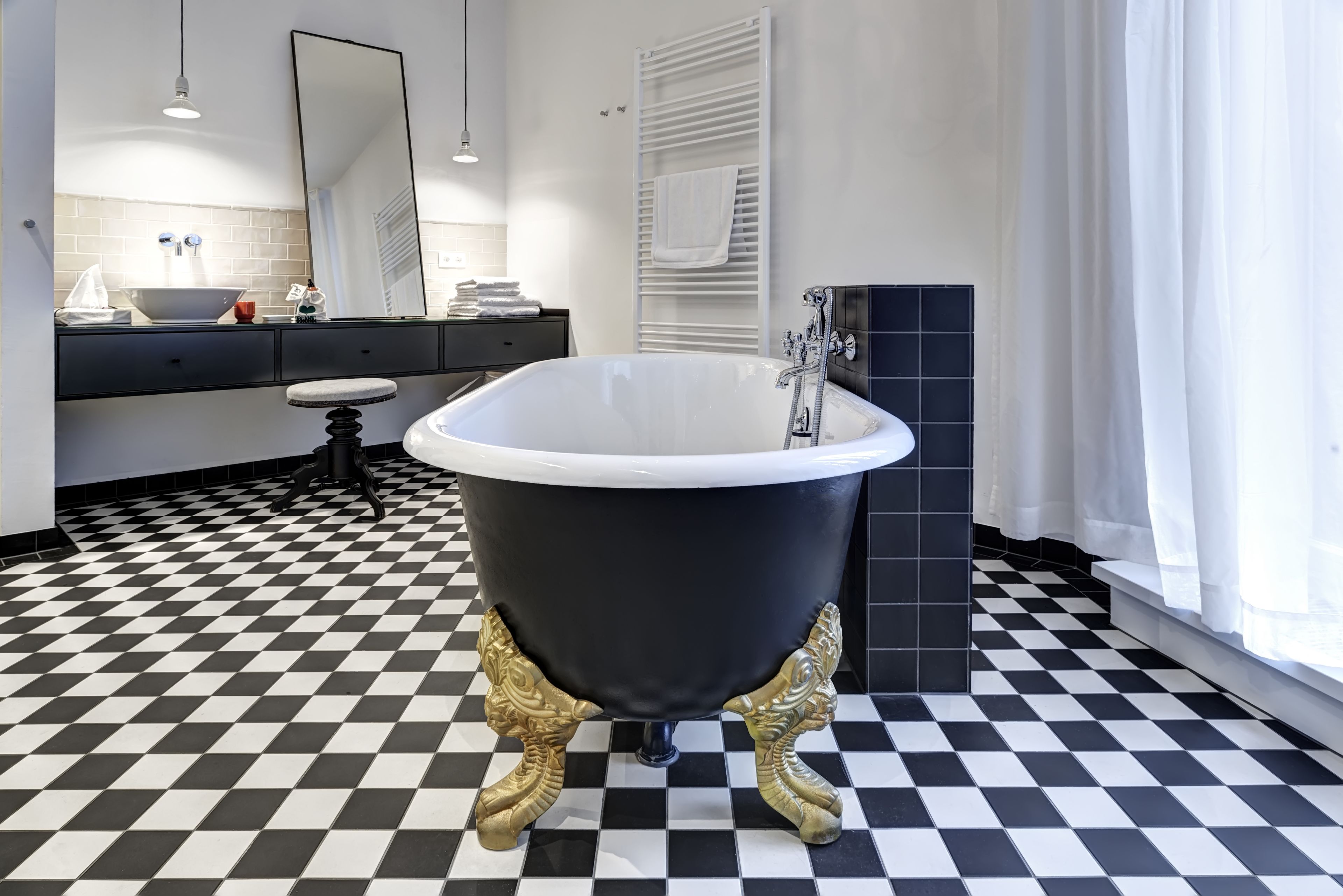A bathroom with a black bathtub, white tiles, a checkered floor, and a large mirror.