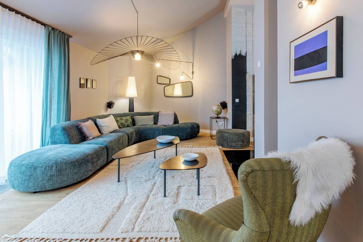 A modern living room with a sectional sofa, a round coffee table, and a green armchair. There is a globe on a small table and a painting on the wall.