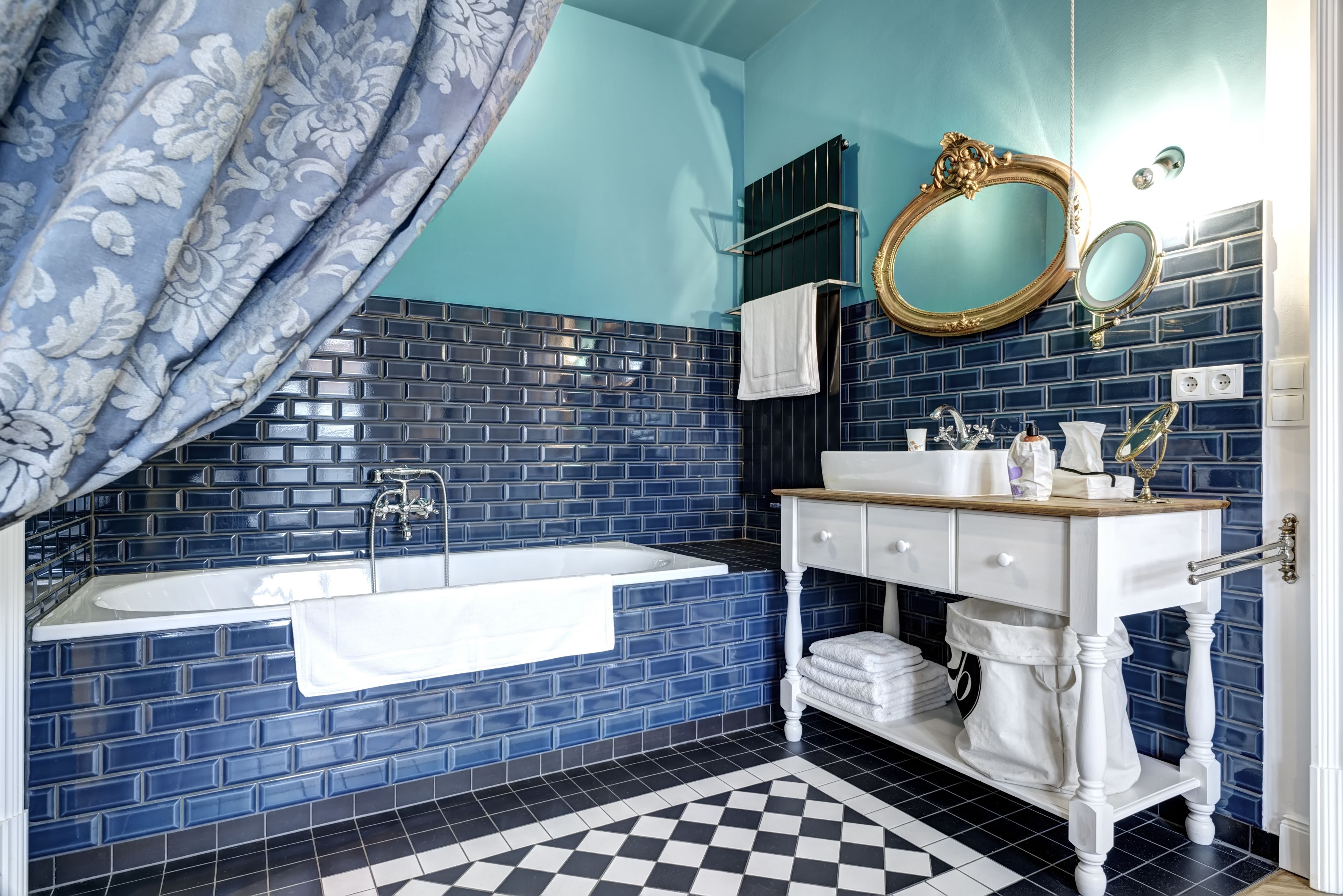 A bathroom with a blue tiled wall, a white vanity, a bathtub, and a checkered floor.