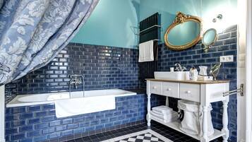 A bathroom with a blue tiled wall, a white vanity, a bathtub, and a checkered floor.