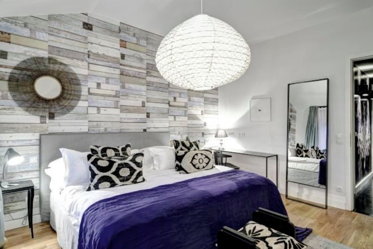 Une chambre moderne avec un lit, des coussins à motifs, un miroir rond et un décor mural original.