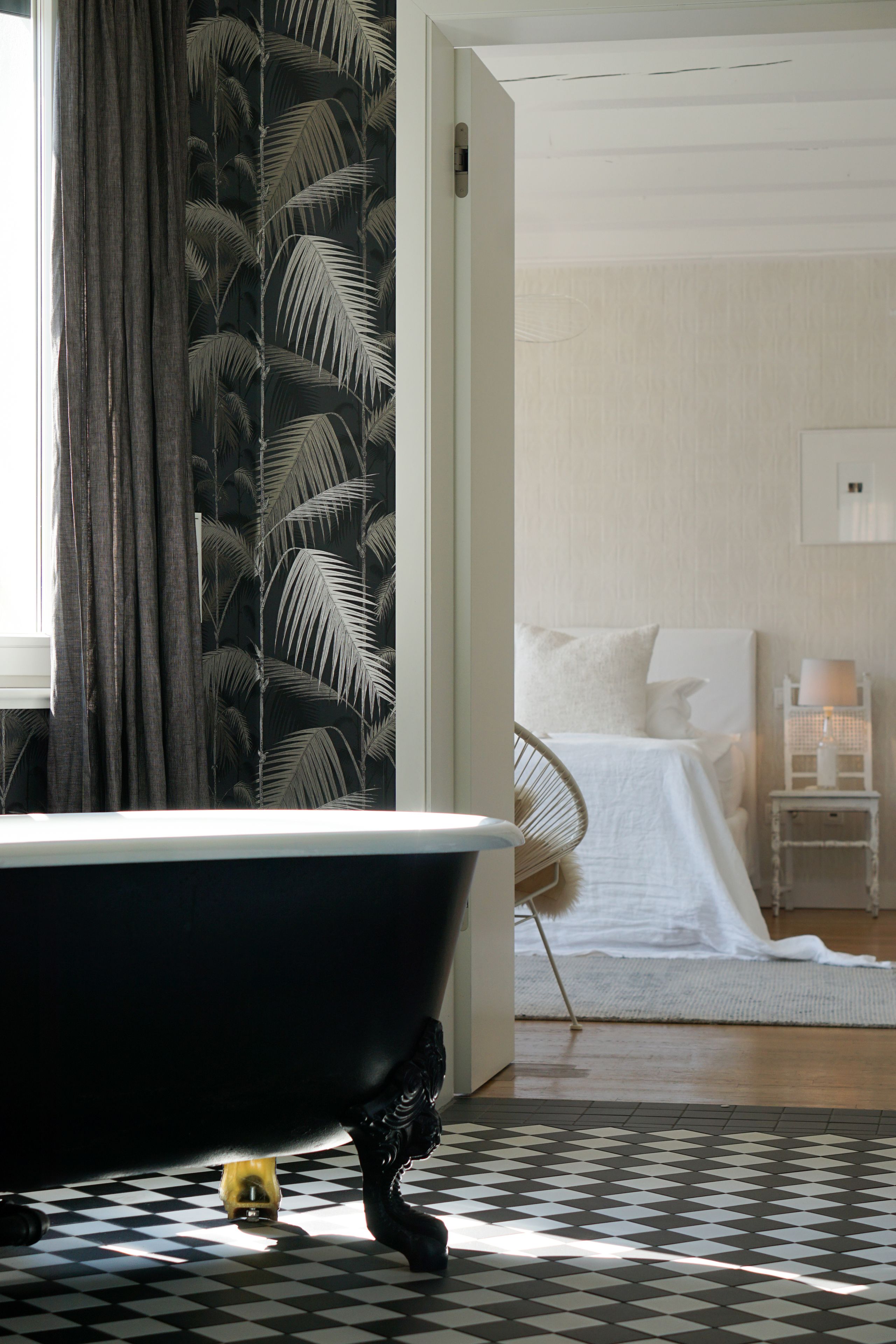 Une salle de bain avec une baignoire noire, un carrelage à carreaux et une fenêtre avec des rideaux.