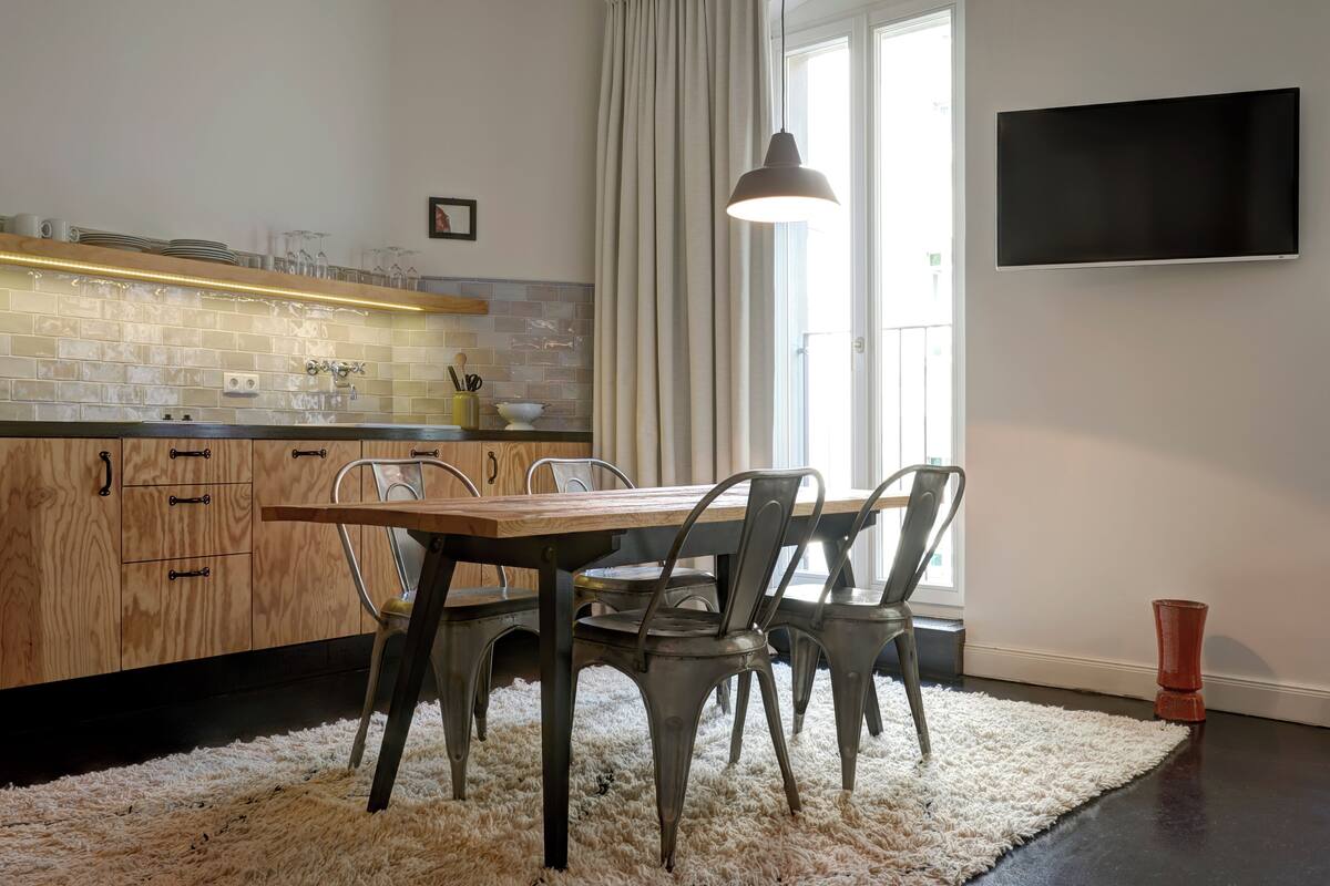 A modern kitchen with a wooden table and chairs, a tiled backsplash, and a flat-screen TV mounted on the wall.
