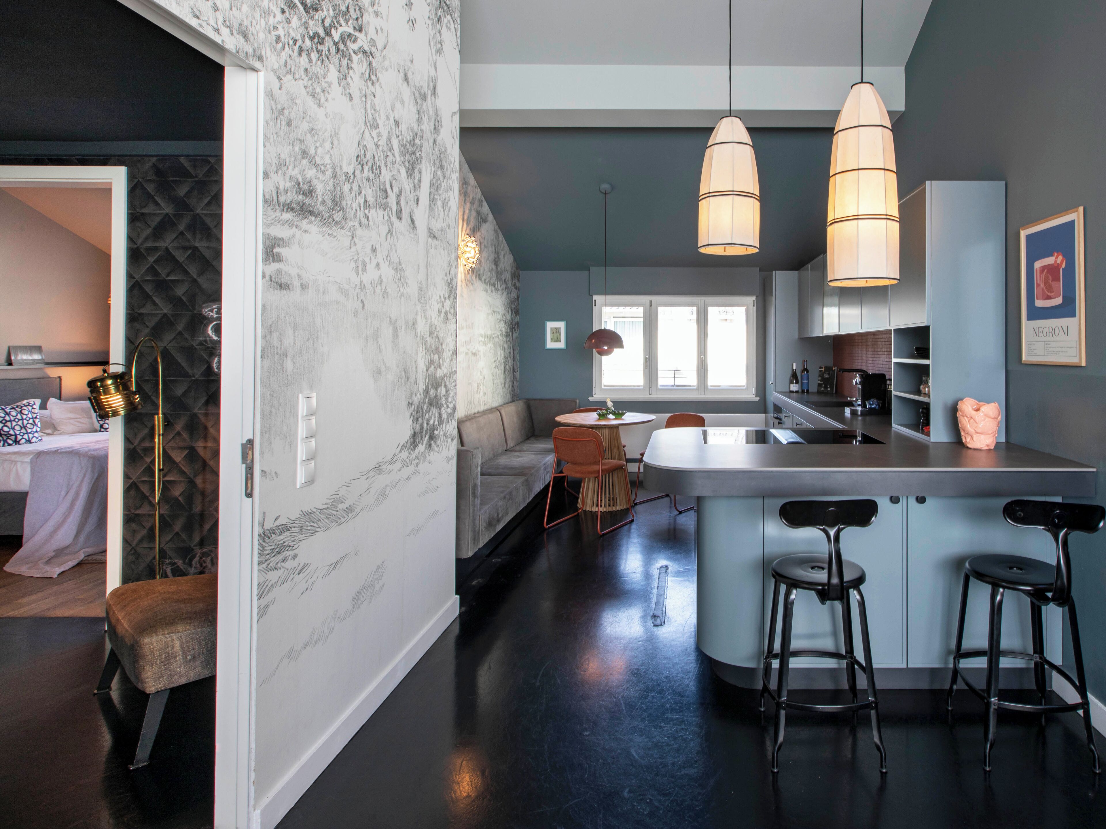 Una cocina moderna con una isla central, taburetes de bar, iluminación colgante y vistas al área de estar contigua.