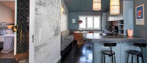 Una cocina moderna con una isla central, taburetes de bar, iluminación colgante y vistas al área de estar contigua.